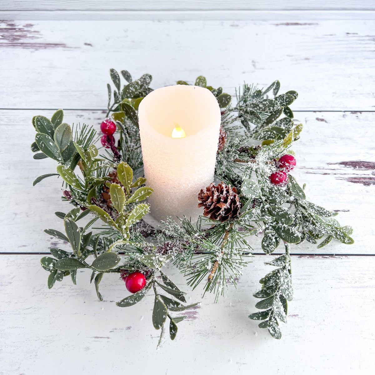 a lit candle surrounded by greenery and berries